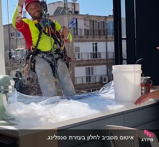 עובד בגובה עם קסדה ורתמה מנופף לשלום